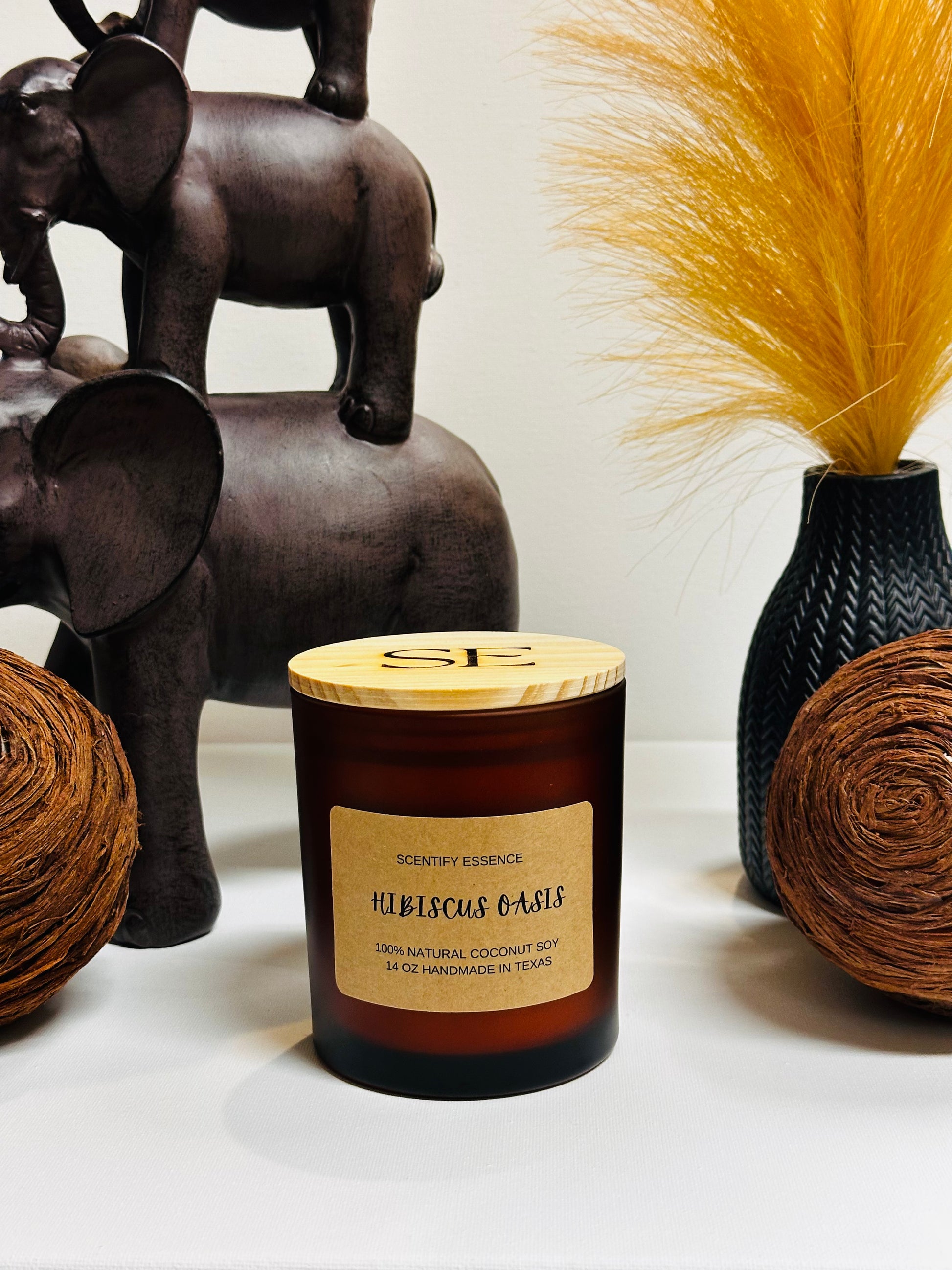 Scentify Essence hibiscus-scented candle in a rose-pink glass jar with floral accents and soft tropical glow.